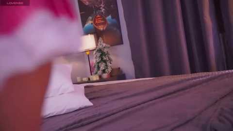 Video of a cozy bedroom with a bed covered in brown and white sheets, a floral artwork on the wall, and a potted plant on a nightstand.