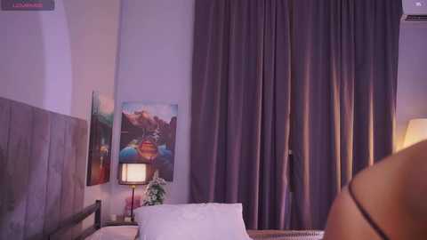 Video of a cozy, dimly lit bedroom with a bed, purple curtains, colorful landscape painting, bedside lamp, and partial view of a person's bare back.