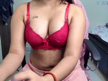 Video of a woman in a red lace bra, revealing her medium-sized breasts and a tattoo on her left shoulder. She is sitting on a chair in a simple room with a pink blanket draped over her lap.