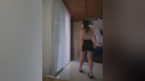 A blurry video of a woman in a white top and black skirt walking away from the camera, standing in a narrow hallway with beige walls and wooden ceiling.