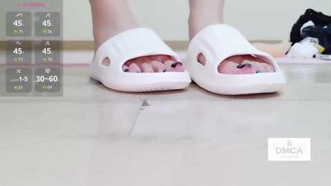 Video of a person's feet wearing white slippers, with a cracked sole on one slipper. Background shows a wooden floor and a black and white toy in the corner.