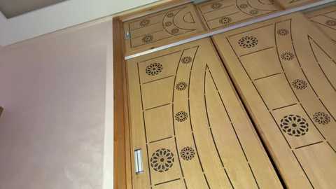 Video of intricately carved wooden closet doors featuring a floral design, set against a light beige wall, with a metallic handle visible on the left side.