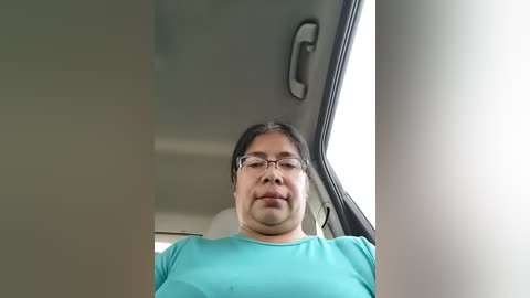 Video of a middle-aged Asian man with glasses, wearing a teal t-shirt, seated in a car. The background shows the car's interior and a window with natural light.