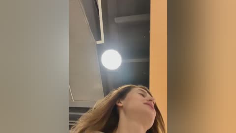Video of a young woman with long, light brown hair, standing with eyes closed, in a modern, industrial setting with exposed concrete ceiling and warm lighting.
