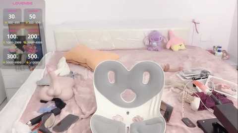 Video of a cluttered bedroom with a white bed, pink blanket, scattered clothes, toys, and electronic devices, including a Nintendo Switch.