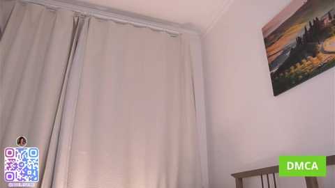 Video of a minimalist room with beige curtains covering a window, a wooden crib in the foreground, and a colorful painting of a sunset on the wall.