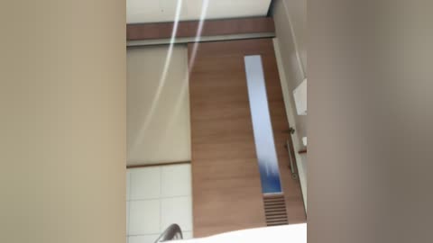 A video of a modern, minimalist interior with a wooden floor, white walls, and a large, rectangular skylight. The image is taken from a low angle, slightly tilted, with a blurry foreground.