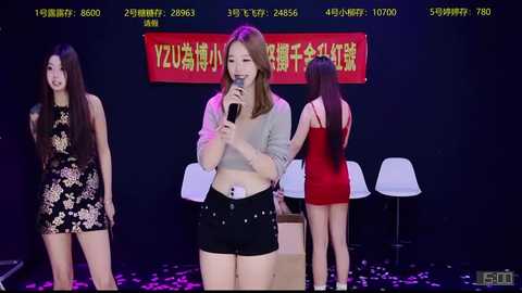 Video of three Asian women onstage: one center singing into a mic in a white crop top and black shorts, another in a black floral dress, and a third in a red dress, all against a dark background with Chinese text.