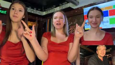 Video of three young women in red tops, making peace signs, in a dimly lit bar with a TV screen showing a woman.