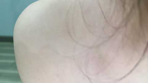 A close-up video of a fair-skinned person's back, showing detailed skin texture and slight discoloration on the buttocks. The background is blurred with a hint of a blue wall and a wooden floor.