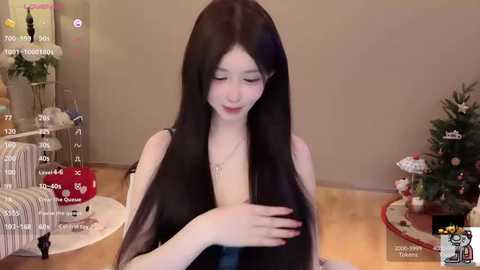 Video of a fair-skinned, long-haired Asian woman with dark hair, seated in a cozy room with a Christmas tree, gifts, and a striped couch in the background.