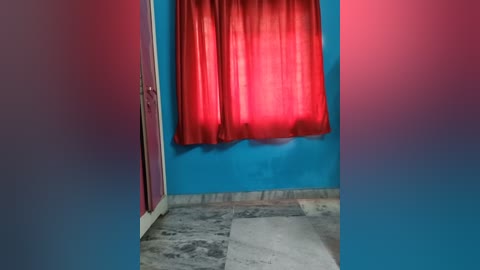 A video of a small, dimly lit room with blue walls, a red curtain, and a marble floor. The room appears empty, with a sense of isolation and minimalism.