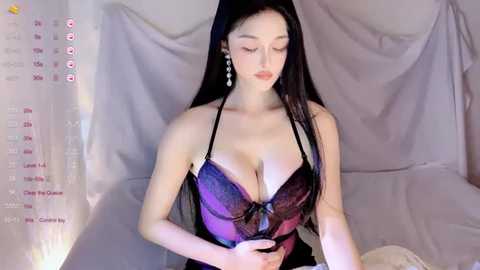 Video of an Asian woman with long black hair, wearing a purple lace bra, standing in a draped room.