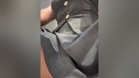 Video of a person wearing a black, pleated skirt with gold buttons and a fitted black top, captured from a low angle. The background is blurred, focusing on the clothing's texture and movement.