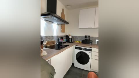 Video of a modern kitchen with white cabinets, black range hood, wooden countertops, gray backsplash, toaster, coffee maker, and a black washing machine.