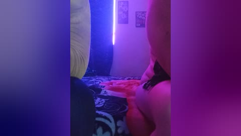 A video captures a nude woman with fair skin and medium-sized breasts, lying on a bed with a patterned sheet. The room is dimly lit with blue and purple LED lights, creating a sensual ambiance.