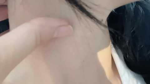 A close-up video of a person's hand gently touching their own bare chest, revealing a mole on the skin. The person has straight, dark hair partially visible, and is wearing a black garment.