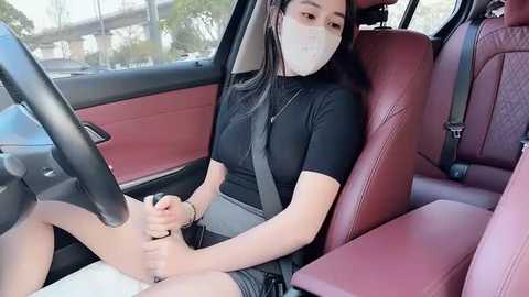 Media: Video of an Asian woman in a black t-shirt, gray skirt, and face mask, sitting in a red car, masturbating with a vibrator, window view of a bridge and trees.