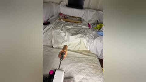A video shows a messy bedroom with white sheets, a wooden rolling pin, and a partially visible yellow toy in the background.