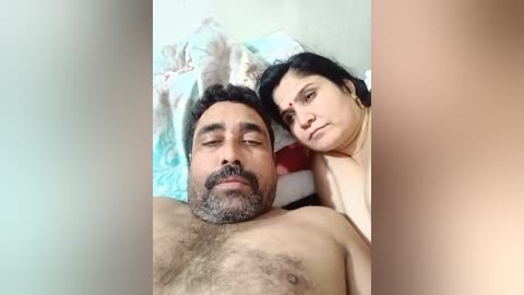 Video of a South Asian man and woman sleeping together on a bed, both with light to medium skin tones. The man has a beard and the woman has a bindi.