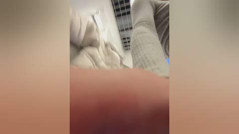 A blurry, close-up video of a person's upper torso in a beige sweater, with a grid-patterned ceiling in the background.