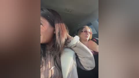 Video of two women in a car; one with long dark hair, the other with glasses and blonde hair, both looking out windows.