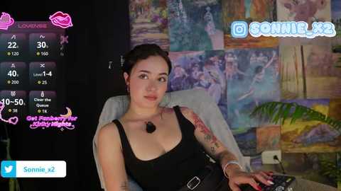 Video of a young woman with fair skin, dark hair, wearing a black tank top and black belt, seated in a chair. Background features colorful, abstract art and social media icons.