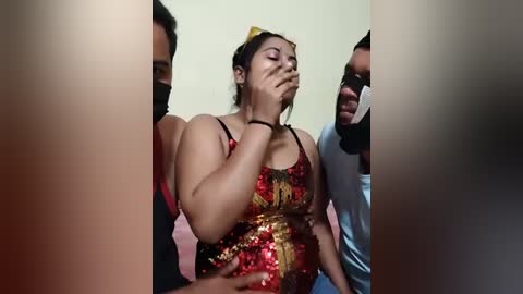 Video of a distraught woman in a red sequined dress, covered in blood, being comforted by men in masks, in a dimly lit room.