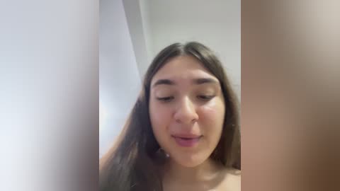 A video of a young woman with long, dark hair and light skin, looking serene with closed eyes, standing in a dimly lit bathroom.