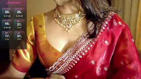 Video of a woman wearing a vibrant, gold and red saree with intricate embroidery, adorned with a gold necklace, set against a warm, indoor background.