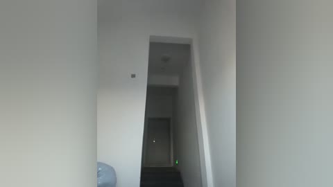 A video of a narrow, dimly lit hallway with white walls, a water dispenser on the left, and a door with a green light at the end.