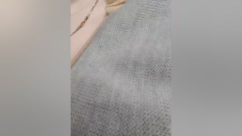Close-up video of a beige fabric with a textured pattern, partially obscured by a blurred background, showcasing a soft, light grey knit material.