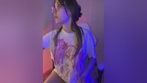 Video of a young woman with long, dark hair, wearing glasses, a white graphic tee, and sitting against a purple backdrop, with soft lighting creating a dreamy atmosphere.