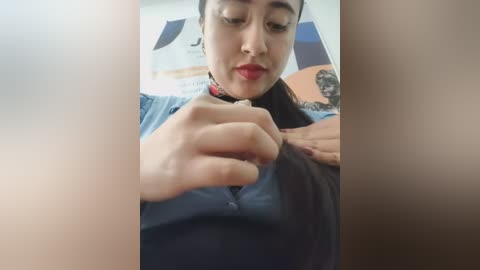 A video shows a woman with medium skin tone and dark hair, wearing a blue shirt, examining her hair with a comb. The background is blurred, featuring a desk with papers.