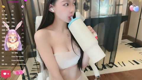 A young Asian woman with long black hair, wearing a white strapless bra, drinks milk from a bottle in a modern room with a digital display of her vitals.