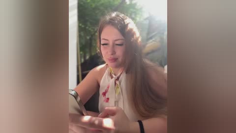 Video of a woman with long brown hair in a sleeveless white blouse, measuring a man's blood pressure. Background shows greenery and a blurred man.