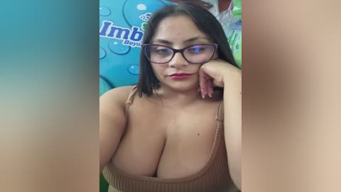 Video of a curvaceous Latina woman with long black hair, wearing glasses and a low-cut brown top, posing in a playful, seductive manner against a colorful, abstract background.