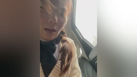 Video of a young girl with light brown hair, wearing a beige jacket, crying while seated in a car. Sunlight filters through the window, creating a bright, blurry background.