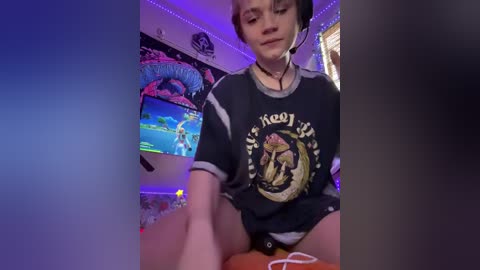 Video of a young gamer with short hair, wearing headphones and a dark t-shirt, sitting in a dimly lit room with gaming setups and colorful decor.