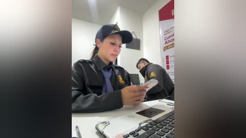 Video of two female police officers in uniforms, one holding a phone, in a brightly lit office with computer and documents.