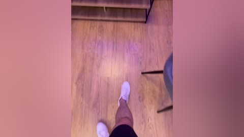 Video of a pair of white socks on a wooden floor, seen from above. The background includes a dark chair and a blurry corner, creating an intimate, slightly voyeuristic scene.