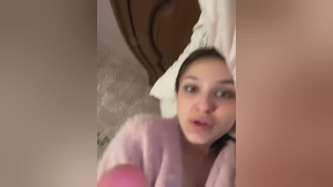 A blurry video of a young woman with dark hair, wrapped in a white towel, peering through a window. She has a surprised expression.