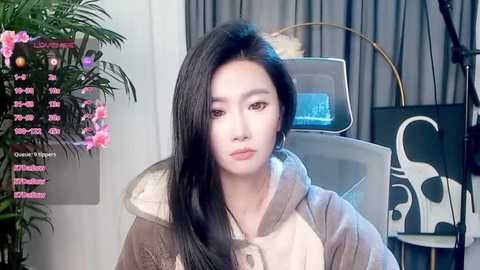 Video of a young Asian woman with long black hair, fair skin, and delicate features, wearing a beige coat, seated in a modern office chair.