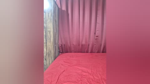 Video of a simple bedroom with a red bedspread, pink curtains, and a beige wall. The room has a cozy, intimate feel with soft, muted colors.