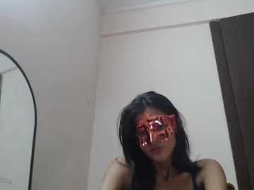 Video of a young woman with long, dark hair, wearing a red, leopard-print face mask, in a dimly lit room with white walls and a partially visible mirror.