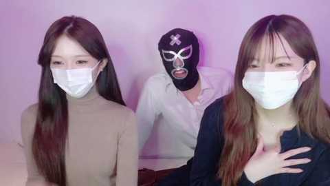 A video featuring three Asian women with long hair in different outfits, one wearing a surgical mask, standing against a lavender background.