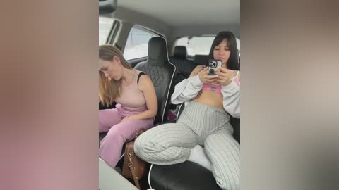 Video of two young women in a car; one in a pink dress, the other in striped pants, holding a camera.
