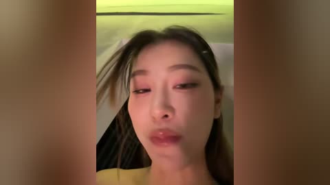 Video of an Asian woman with long, straight black hair and light skin, wearing pink eyeshadow, making a pouty face. Background shows a beige wall and a dark curtain.