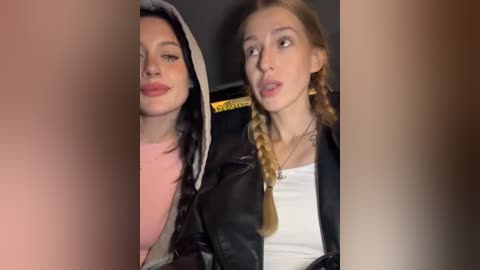 Media: Video of two young women with pale skin and light hair, wearing casual clothes, seated in a car, looking slightly to the side.