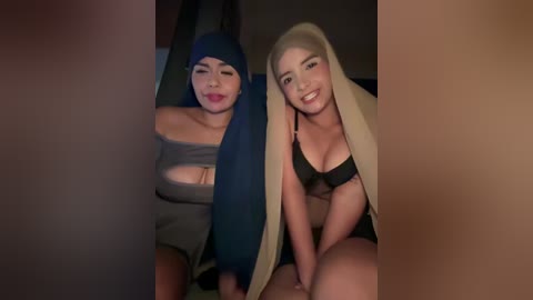 A video of two women, one in a blue hijab, the other blonde, posing in lingerie, smiling, partially obscured by a blurred figure.